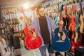 Picture of young hipster stand and hold two colorful acoustic guitars. They are red and dark-blue colors. Guy look at Royalty Free Stock Photo