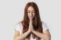 Picture of young redhead female isolated on grey background, having put hands together in prayer, looking relaxed and calm,