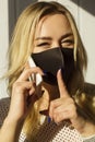 Picture of young blond woman wearing black protection mask at daylight