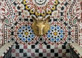 Closeup of a mosaic fountain with geometric Arabic design and stag head faucet on display at Art Naji in Fez, Morocco.