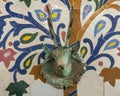 Closeup of a mosaic fountain with geometric Arabic design and stag head faucet on display at Art Naji in Fez, Morocco.