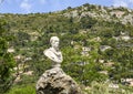 Marble bust perched high on a rock, seen from the road exiting the medieval village of Eze, France