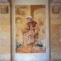 Mural painted on a wall featuring a young woman in a turban sitting with flowers at her feet and wearing a transparent COVID mask.