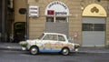 Antique white car with paintings of Genoa, flags of Genoa, and flower pots.