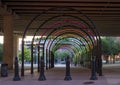 Walkway under a freeway in downtown dallas, with multi-colored lights in arches.