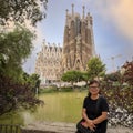 Korean female tourist with a small lake and the East facade of the Basilica de la Sagrada Familia in Barcelona, Spain.l