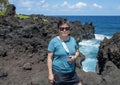 Female Korean tourist standing on rugged lava shoreline next to the Black sand beach on the Island of Maui in the State of Hawaii.