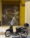 Black motorbike parked on the street in front of a graffiti style mural in Bologna, Italy.