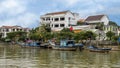 Three wooden fishing boats along the bank of the Thu Bon River in Hoi An, Vietnam, with hotel in the background