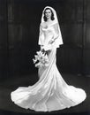 Twenty year-old bride in 1944 in a full length classic wedding dress holding white flowers.