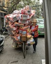 Vietnamese street vendor in Hanoi, on bicycle carrying goods for sale.