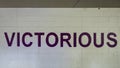 Victorious is painted in bold purple letters on a white brick wall in the parking garage on Victory Park Lane, Dallas, Texas