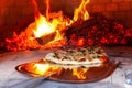 Man is placing a freshly prepared pizza into an outdoor bread oven -