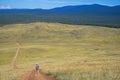 Picturesque amazing landscape of steppe, forest and mountains with small figure of young tourist girl walking away country road