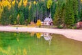 Picturesque autumn scenery of historic chapel reflected in water of Lago di Braies in the Dolomites, Italy