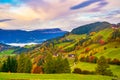 Picturesque autumn scenery with meadows, foliage trees and mountain hills under colorful clouds