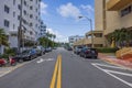 Picturesque cityscape of one of Miami Beach streets with parked cars on both sides, on blue sky with rear white clouds background.
