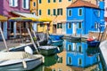 Picturesque colorful idyllic scene with a boats docked on the water canals in Burano Venice Italy. Water reflection