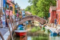 Picturesque colorful idyllic scene with a boats docked on the water canals and tourists strolling in Burano Venice Italy. Water