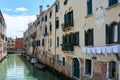 Picturesque facades of old buildings with hanging clothes and boats parked on canal in Venice, Italy, under blue sky with clouds o Royalty Free Stock Photo