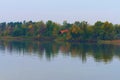 Picturesque landscape of autumn colored trees are reflected in the water. Wooden house with red tile roof is hidden in the forest Royalty Free Stock Photo