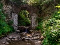 Old stone arched destroyed bridge over small river in a mountain forest