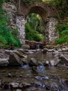 Old stone arched destroyed bridge over small river in a mountain forest