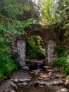 Old stone arched destroyed bridge over small river in a mountain forest