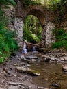 Old stone arched destroyed bridge over small river in a mountain forest