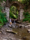 Old stone arched destroyed bridge over small river in a mountain forest