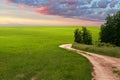 A picturesque rural landscape at sunset. A green field with a winding field road under heavy rain clouds. Copy space. Royalty Free Stock Photo