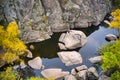 A picturesque stream flows in the Aktovsky Canyon, surrounded by autumn trees and large stone boulders