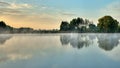 A picturesque sunrise over a foggy lake with trees on the shore reflected in the water. Morning of the end of summer, beginning of Royalty Free Stock Photo