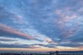 The picturesque sunset sky with blue-orange clouds in the form of stripes over a city. Scenic view of the skyscape at evening