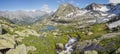 A picturesque valley in the Altai Mountains. Green alpine meadows, spring flowers, snow, lakes and creek. Panorama