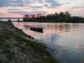 Picturesque view of the Sava River in Bosanski Brod with a broken dock, a boat in the water and the silhouette of a bridge in the
