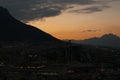 Picturesque view of sunset with dark clouds above big mountains and evening city