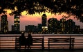 Picturesque view of a sunset over the city skylines and a couple's silhouettes sitting on a bench Royalty Free Stock Photo