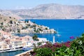 Picturesque view on tiny colorful houses on rocks and boats through blooming plants on balcony near the Mediterranian sea on Greek