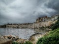 Picturesque view of the wall of old town and houses on the hill on the coast under cloudy sky, Malta Royalty Free Stock Photo