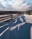 Picturesque waved shadows on snow from wood fence. Alpine mountain winter hamlet outskirts, snowy path, fir forest. High Royalty Free Stock Photo