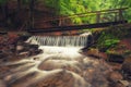 Picturesque wooden bridge across a stream in the middle of a deciduous green summer forest. Crossing a small river. Spring Royalty Free Stock Photo