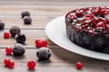 Pie with berries: raspberry, currant, strawberry on a white plate on a wooden background, near red currant and cherry Royalty Free Stock Photo