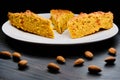 Pie on a big plate and almonds. Pieces of cake with nuts on a wooden dark background. Baking orange with nuts on a wooden table
