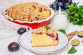 Pie with plums and shtreisel on a plate on a white wooden background. Royalty Free Stock Photo