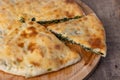 Pie with spinach, herbs and suluguni cheese on a wooden board. Whole pie with cut off piece. Traditional round flat pie.