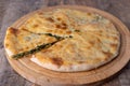 Pie with spinach, herbs and suluguni cheese on a wooden board. Whole pie with cut off piece. Traditional round flat pie.