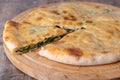 Pie with spinach, herbs and suluguni cheese on a wooden board. Whole pie with cut off piece. Traditional round flat pie with