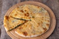 Pie with spinach, herbs and suluguni cheese on a wooden board. Whole pie with cut off piece. Traditional round flat pie.