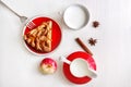 A piece of apple cake with cinnamon, fresh apple, milk cup and jug on the light wooden table. Top view